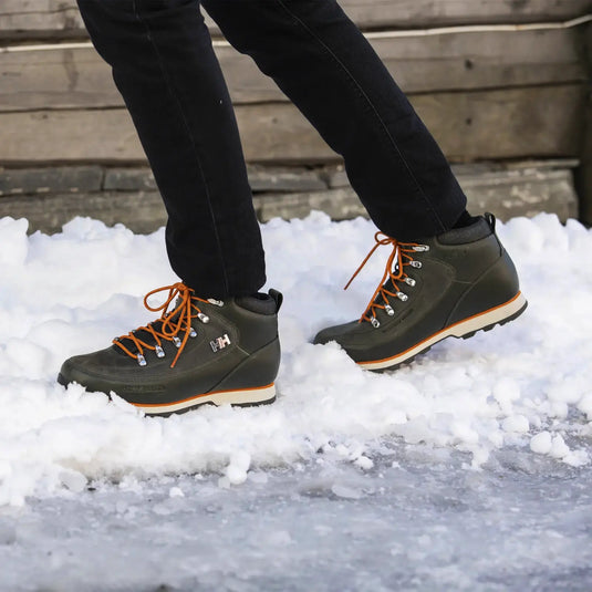 Person, die dunkle Helly Hansen® Men's Forester Winterstiefel trägt, geht auf Schnee.