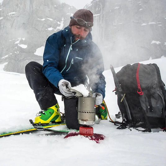 Ein Bergsteiger schmilzt Schnee auf einem MSR® Reactor® Kochsystem, dem effizientesten Kochsystem, für Wasser inmitten von schneebedeckten Bedingungen.