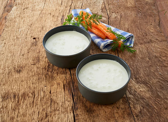 Zwei Schalen mit cremiger Suppe, Karotten und Kräutern auf Holz.