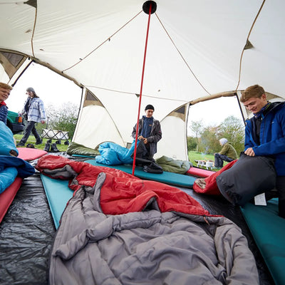 Eine Gruppe von Menschen baut einen Campingplatz mit Schlafsäcken und Matten in einem großen Grand Canyon® Hattan 5.0-Zelt auf.