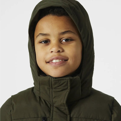 Junge Person, die einen grünen Adore Puffy Parka von Helly Hansen® Juniors trägt, lächelt in die Kamera.