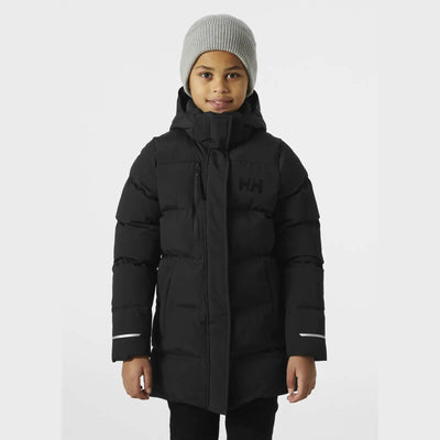 Kind trägt einen schwarzen wattierten Wintermantel „Adore Puffy Parka“ von Helly Hansen® Juniors und eine graue Mütze.