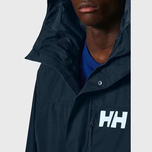 Eine Person, die einen Helly Hansen® Men’s Rigging Insulated Raincoat mit dem „hh“-Logo über einem blauen Hemd trägt.