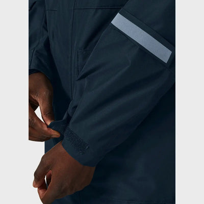 Person in einem dunkelblauen Helly Hansen® Men’s Rigging Insulated Raincoat mit einem reflektierenden Streifen am Ärmel, der die Manschette reguliert.