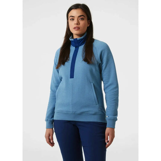 Frau trägt einen blauen Rollkragenpullover „Women's Lillo Outdoor Sweater“ von Helly Hansen® und eine passende Hose.