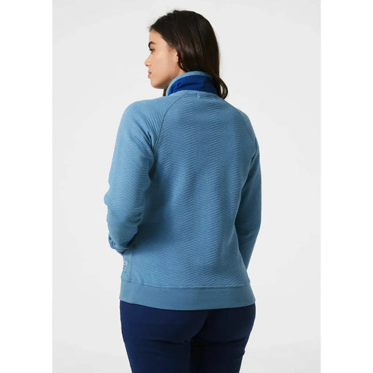 Eine Frau von hinten trägt eine blau strukturierte Jacke von Helly Hansen® Women's Lillo Outdoor Sweater und eine dunkelblaue Hose.