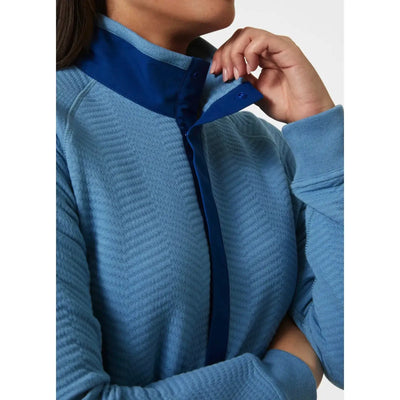 Nahaufnahme einer Person, die den Kragen eines Lillo Outdoor-Pullovers für Damen von Helly Hansen® mit kontrastierendem blauen Innenfutter anpasst.