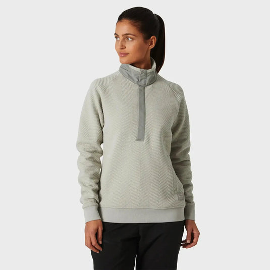 Frau trägt einen hellgrauen Rollkragenpullover „Women's Lillo Outdoor Sweater“ von Helly Hansen® mit halbem Reißverschluss vorne, gefertigt aus Bio-Baumwolle.