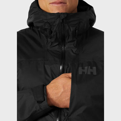 Eine Person, die eine schwarze Helly Hansen® Men’s Verglas 2L Shell Jacket trägt und deren Hand teilweise in der Jacke steckt.