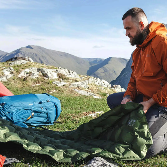 Mann baut einen Campingplatz in den Bergen HIGHLANDER NAP-PAK Aufblasbare Isomatte, XL auf.