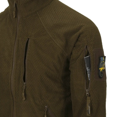 Nahaufnahme einer braun strukturierten Helikon-Tex® Alpha Tactical Jacket – Grid Fleece mit einer Reißverschlusstasche und einem Aufnäher am Ärmel.