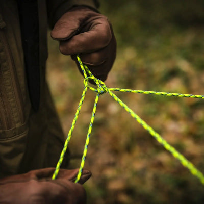 Person, die einen Knoten in einem gelb-grünen Atwood Rope MFG™ Paracord 550 (30 Meter) knüpft.