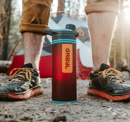 Ein Camper steht mit einer Wasserflasche zwischen seinen Füßen.