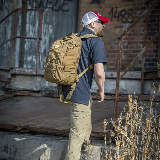 Mann mit Helikon-Tex® EDC-Rucksack – Cordura (21 Liter) steigt die Stufen vor einem mit Graffiti verzierten Gebäude hinauf.