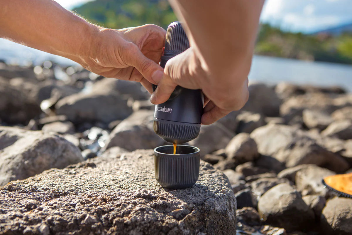 Hände bedienen tragbare Kaffeemühle über Tasse im Freien.