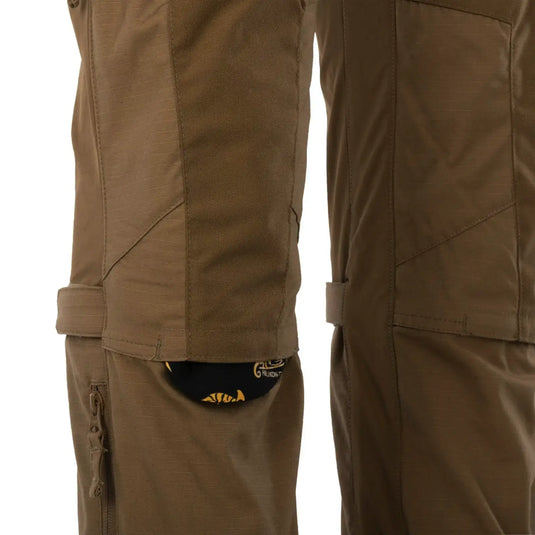 Nahaufnahme einer braunen Helikon-Tex® PATRIOT MCDU PANTS mit einem Taschendetail, das einen darin verstauten schwarzen und gelben Handschuh zeigt.