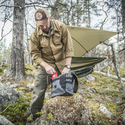 Mann packt seine Ausrüstung in eine Helikon-Tex® Bushcraft Haversack Bag – Cordura in der Nähe einer Hängematte in einem Wald.