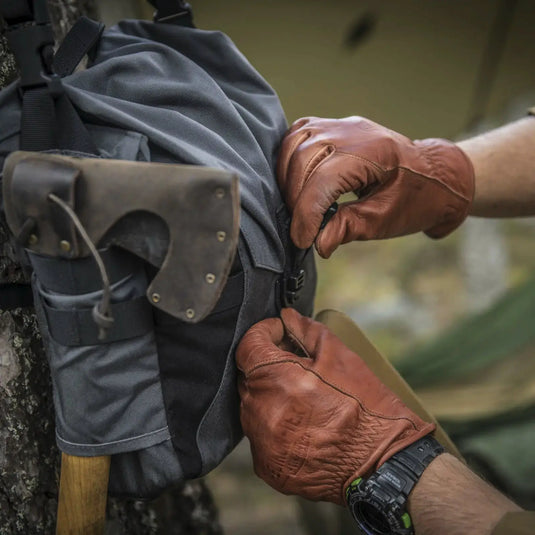 Eine Person sichert im Freien eine graue Helikon-Tex® Bushcraft Haversack Bag – Cordura mit einem daran befestigten Beil.