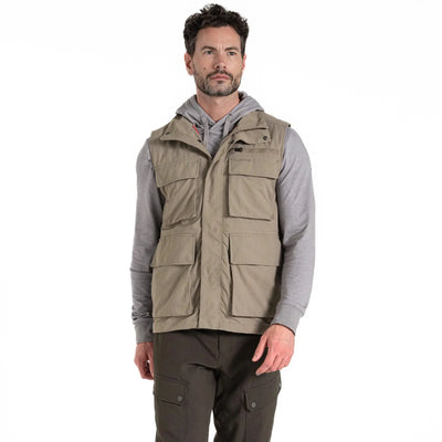 Ein Mann trägt einen grauen Kapuzenpullover unter einer ärmellosen khakifarbenen Craghoppers NosiLife Adventure Gilet IV für Herren, gepaart mit einer passenden Cargohose.