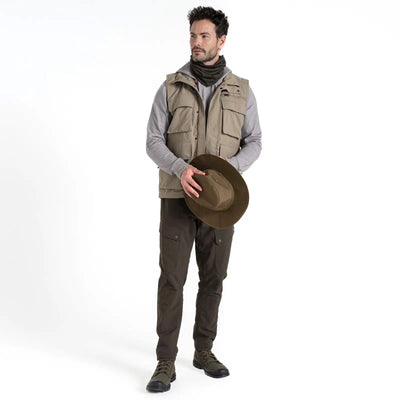 Mann steht in Outdoor-Ausrüstung mit einer Craghoppers NosiLife Adventure Gilet IV für Herren und einem Hut in der Hand.