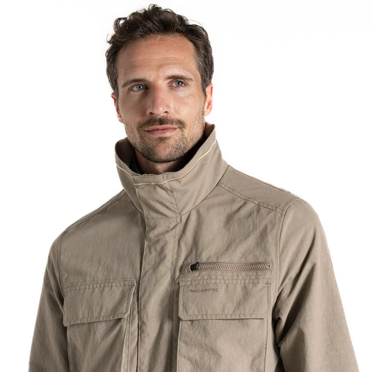 Mann trägt eine beige Craghoppers NosiLife Adventure Jacket IV für Herren mit Reißverschlusstasche und blickt in die Kamera.