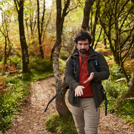 Ein Mann mit einem Craghoppers NosiLife Adventure Jacke IV für Herren-Rucksack, der beim Spaziergang auf einem Waldweg auf seine Smartwatch schaut.