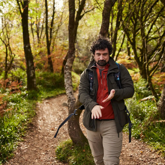 Ein Wanderer überprüft seinen Craghoppers NosiLife Spry Jacke für Herren Fitness-Tracker, während er auf einem Waldweg spaziert.