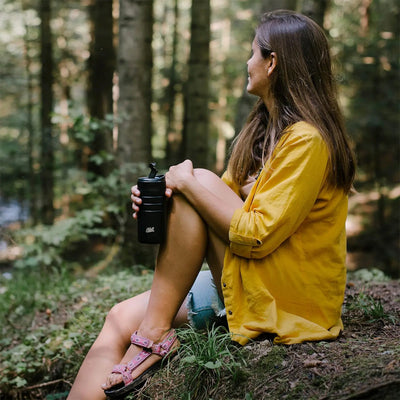 Frau sitzt im Wald und hält einen Esbit® Thermobecher mit Klick-Verschluss 450 ml mit Isoliertechnologie in der Hand und genießt die Natur.