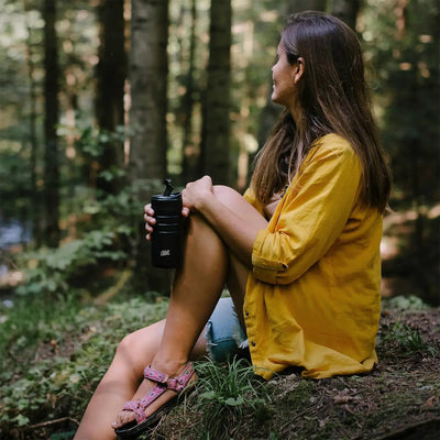 Frau sitzt im Wald und hält einen Esbit® Thermobecher mit Klick-Verschluss 450ml in der Hand, während sie in die Ferne blickt.