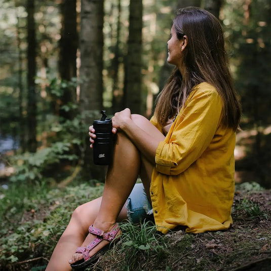 Frau sitzt im Wald und hält einen Esbit® Thermobecher mit Klick-Verschluss 450ml in der Hand, während sie in die Ferne blickt.