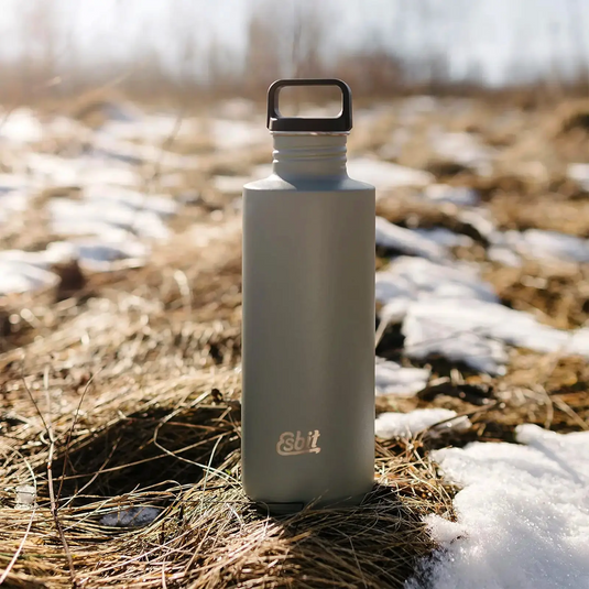 Eine auslaufsichere Esbit® Trinkflasche Sculptor 1000ml Edelstahl steht auf dem Boden mit Flecken von Schnee um sie herum.