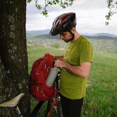 Radfahrer mit Helm prüft im Freien die Esbit® Trinkflasche Sculptor 1000ml Edelstahl in einem roten Rucksack.