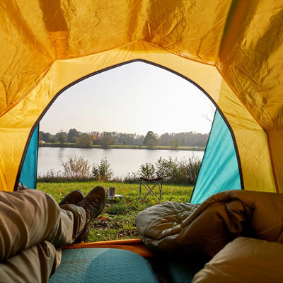 Blick aus dem Inneren eines Zeltes auf eine ruhige Campingszene am Seeufer mit einer Grand Canyon® Hattan 3.8-Matte, die dem Erlebnis Komfort verleiht.