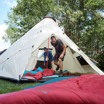 Zwei Camper in der Nähe eines Grand Canyon® Hattan 3.8-Zeltes, ausgestattet mit selbstaufblasenden Grand Canyon®-Schlafsäcken, in einer Waldumgebung.