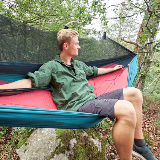 Ein Mann entspannt sich in einer selbstaufblasenden Grand Canyon® Hattan 3.8 Hängematte in einem Waldgebiet.