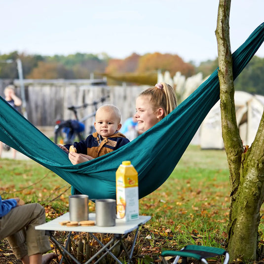 Eine Frau und ein Baby entspannen sich in einer Grand Canyon® Bass Hammock Double im Freien mit Campingausrüstung in der Nähe und Blick auf den Grand Canyon.