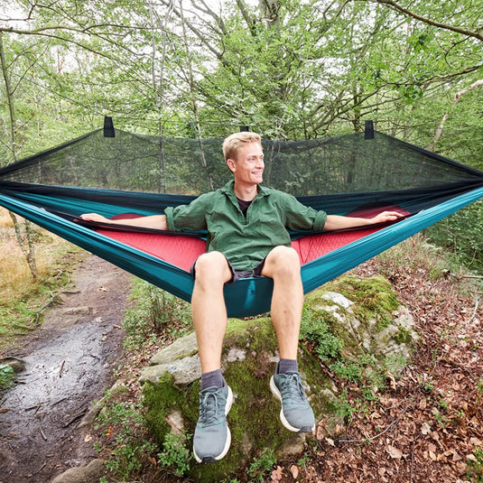 Ein Mann entspannt sich in einer Grand Canyon® Bass Mosquito-Hängematte im Wald.