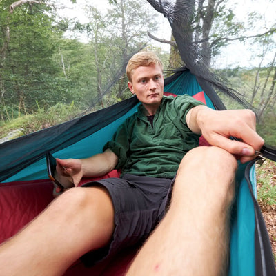 Mann ruht sich draußen in einer Grand Canyon® Bass Mosquito Hammock aus und macht ein Selfie.