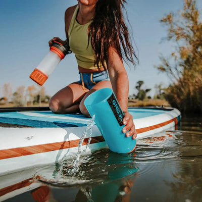 Frau gießt Wasser aus einem Grayl® Geopress Wasserfilter 710 ml auf ein Paddleboard, während sie darauf sitzt.