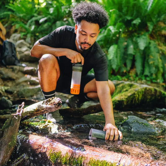 Mann sammelt Wasser aus einem Bach mit einem Grayl Ultrapress Wasserfilter 500 ml für eine effektive Wasserreinigung.