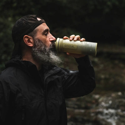 Mann trinkt sauberes Trinkwasser aus einer 500-ml-Wasserflasche von Grayl® Ultrapress Wasserfilter im Freien.