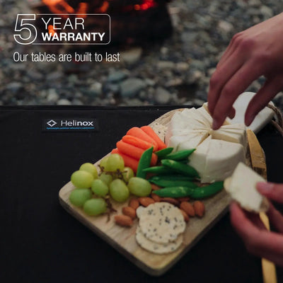 Zubereiten einer Käse- und Gemüseplatte auf einem robusten Helinox Table One Hard Top, ideal für jede Outdoor-Aktivität, mit 5 Jahren Garantie.