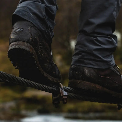 Person, die im Freien auf einer Slackline läuft, mit Fokus auf die schlammigen HIGHLANDER® „Pentland“ Stiefel-Schuhe.