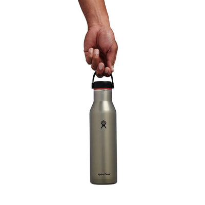 Eine Person hält eine leichte Hydro Flask® 21 oz (621 ml) Lightweight Standard Mouth Trail Series™-Wasserflasche aus Edelstahl am Griff vor einem weißen Hintergrund.