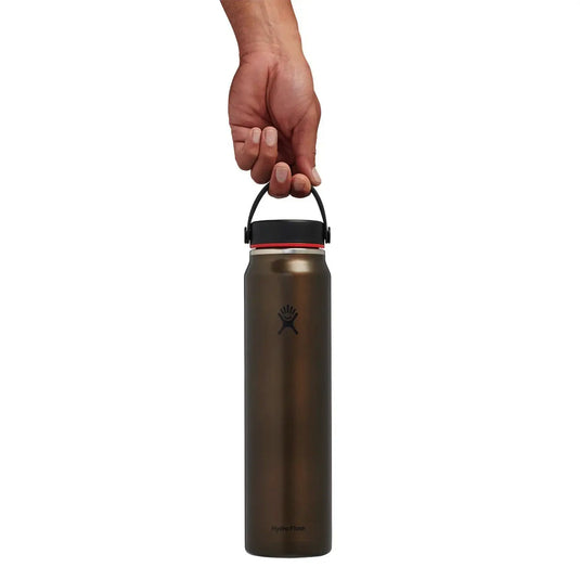 Eine Hand hält eine leichte Hydro Flask® 40 oz (1183 ml) Wide Mouth Trail Series™ Wasserflasche am Griff vor einem weißen Hintergrund.