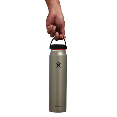 Eine Hand hält eine Hydro Flask® 40 oz (1183 ml) Lightweight Wide Mouth Trail Series™ Wasserflasche am Griff vor einem weißen Hintergrund.