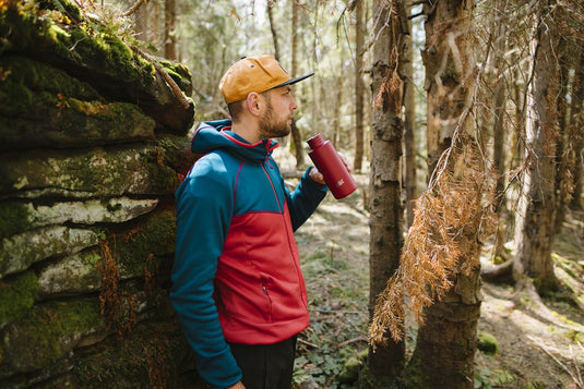 Mann mit einer Wasserflasche steht an einer Steinmauer im Wald.