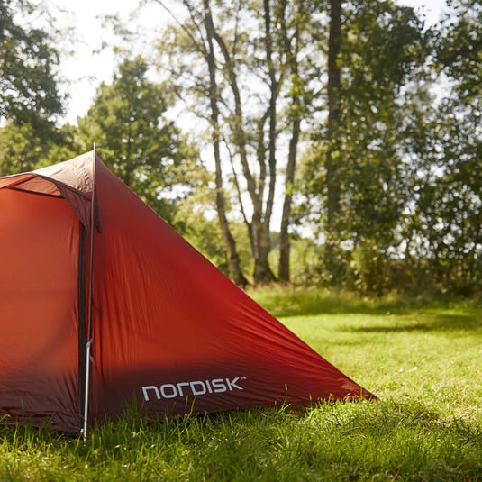 Rotes Campingzelt Nordisk® Lofoten 2 ULW Zelt auf einer Wiese mit Bäumen im Hintergrund.