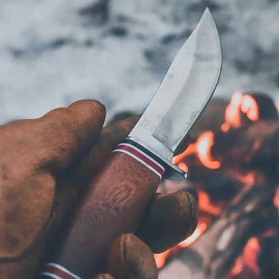 Hand hält ein hochwertiges ØYO Geilo Slirekniv mit einem Feuer im Hintergrund.