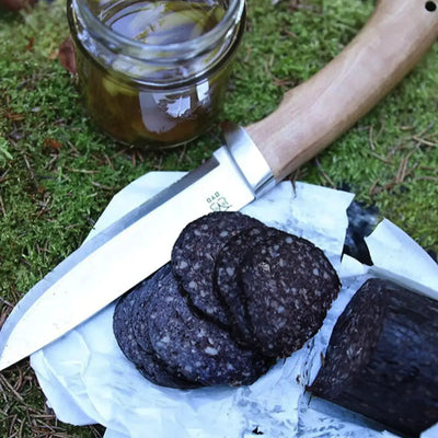 Scheiben Blutwurst neben einem ØYO Rondane Slirekniv und einem Glas Gewürzen auf einem Moosbett.